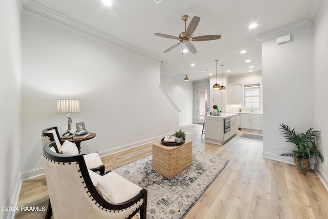 sitting room with light wood-type flooring, ceiling fan, and ornamental molding