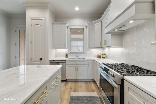 kitchen with custom exhaust hood, white cabinets, sink, appliances with stainless steel finishes, and light hardwood / wood-style floors