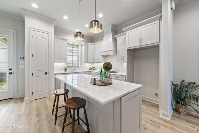 kitchen with premium range hood, light stone counters, sink, a center island, and white cabinetry