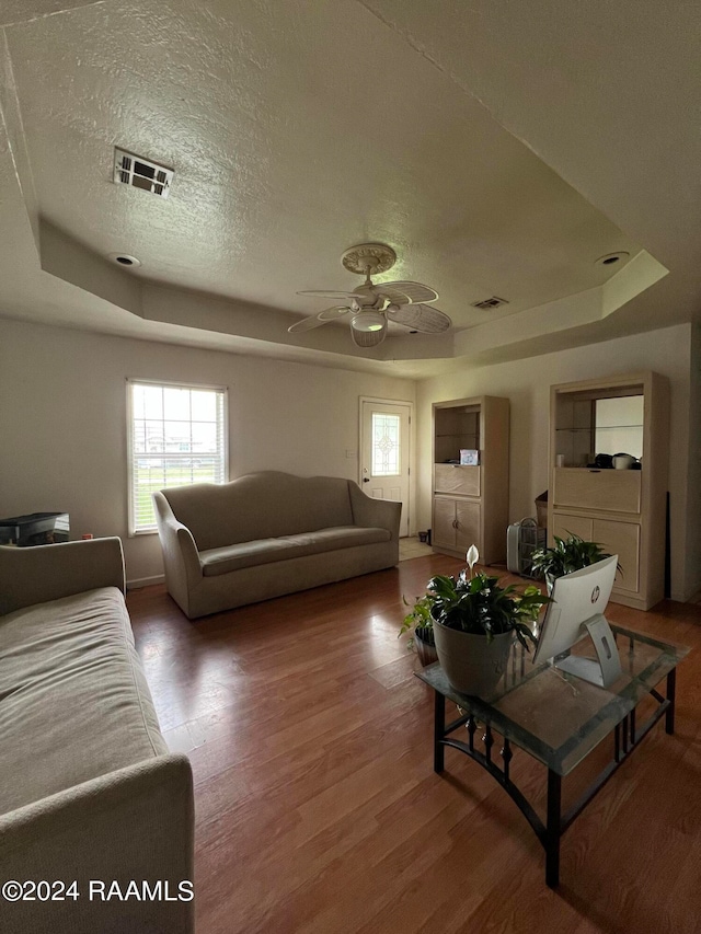 living room with hardwood / wood-style flooring, a textured ceiling, ceiling fan, and a raised ceiling