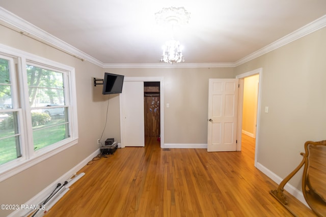 empty room with ornamental molding, a chandelier, and light hardwood / wood-style flooring