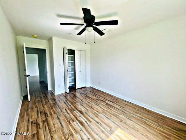 unfurnished bedroom with ceiling fan, dark wood-type flooring, and a closet