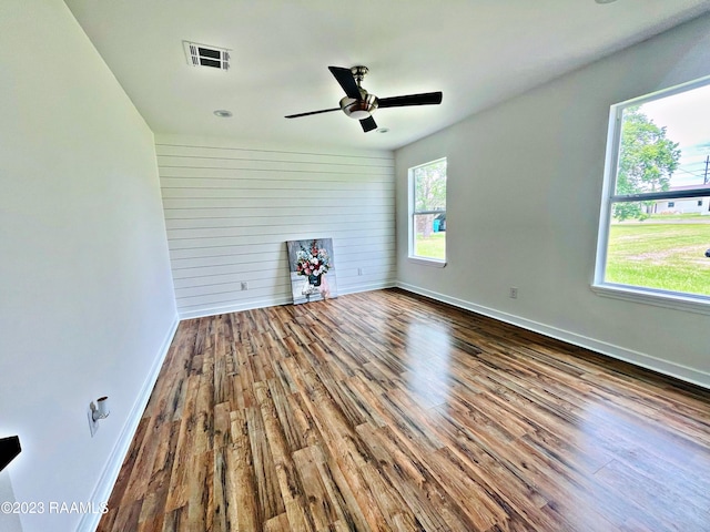 empty room with wood walls, hardwood / wood-style floors, and ceiling fan