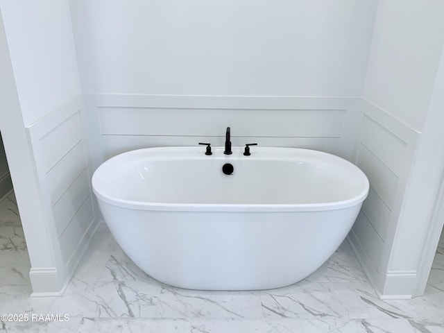 full bath featuring a soaking tub, marble finish floor, and a wainscoted wall