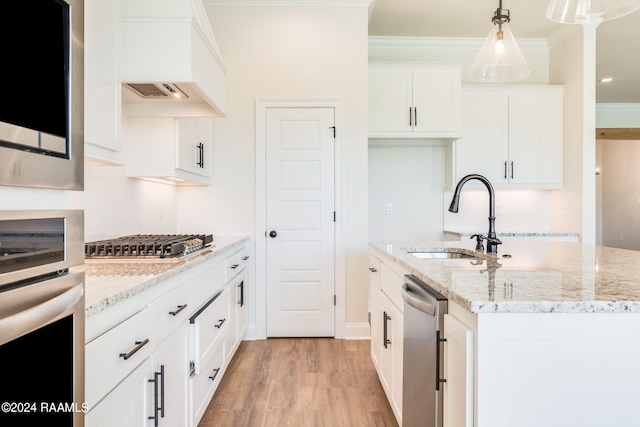 kitchen with an island with sink, ornamental molding, a sink, stainless steel appliances, and light wood finished floors