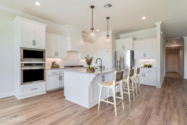 kitchen with visible vents, a kitchen island with sink, light wood-style floors, appliances with stainless steel finishes, and a breakfast bar area