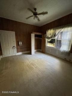 unfurnished living room with ceiling fan and wooden walls