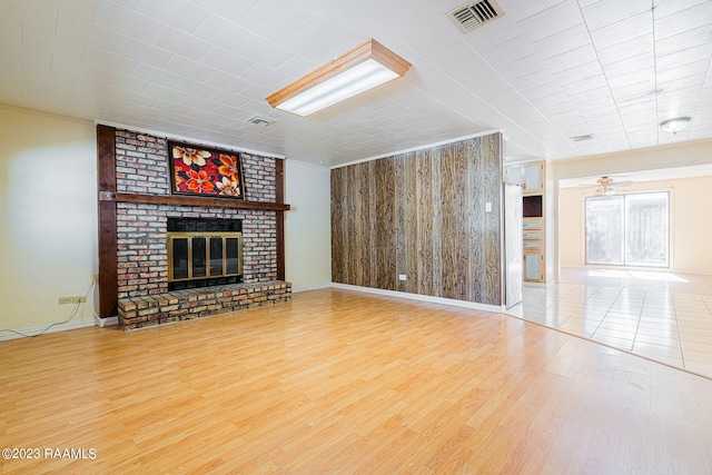 unfurnished living room with brick wall, light hardwood / wood-style floors, a brick fireplace, and ceiling fan