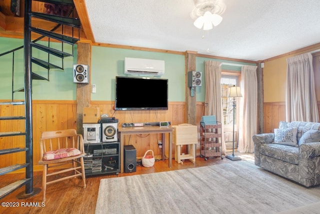 living room with wood walls, a textured ceiling, ornamental molding, a wall unit AC, and hardwood / wood-style floors