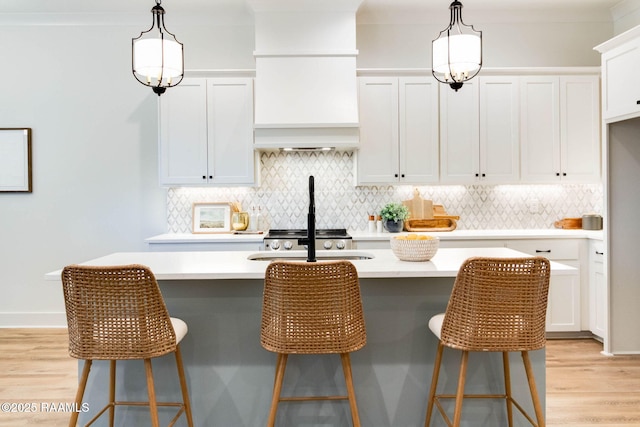 kitchen with decorative light fixtures, a kitchen bar, white cabinetry, and a kitchen island with sink