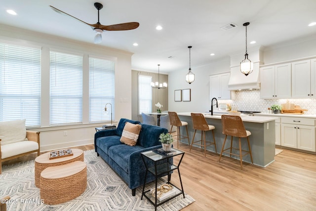 living room with ornamental molding, ceiling fan with notable chandelier, light hardwood / wood-style flooring, and a healthy amount of sunlight