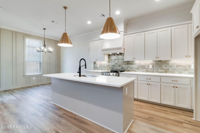 kitchen with white cabinetry, a kitchen island with sink, hanging light fixtures, and sink