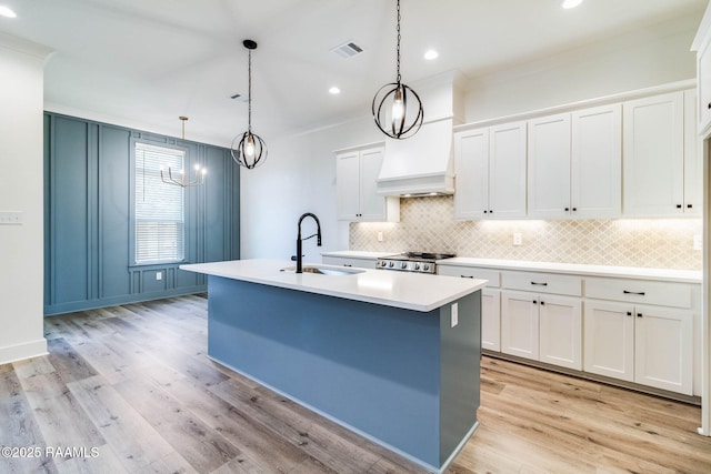 kitchen featuring pendant lighting, white cabinets, a center island with sink, sink, and light hardwood / wood-style flooring