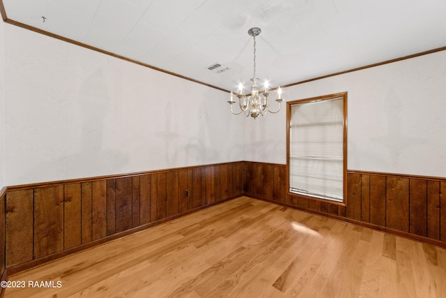 spare room with ornamental molding, an inviting chandelier, light hardwood / wood-style floors, and wood walls