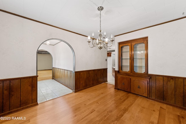 unfurnished dining area with ornamental molding, light wood-type flooring, and wood walls