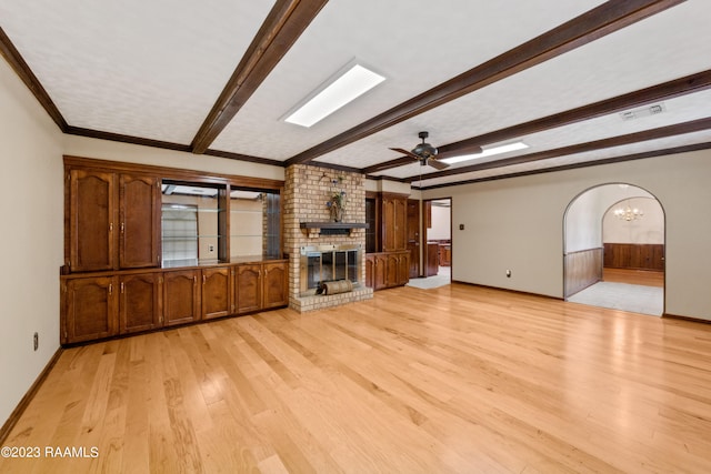 unfurnished living room featuring ceiling fan, beam ceiling, ornamental molding, light hardwood / wood-style floors, and a brick fireplace