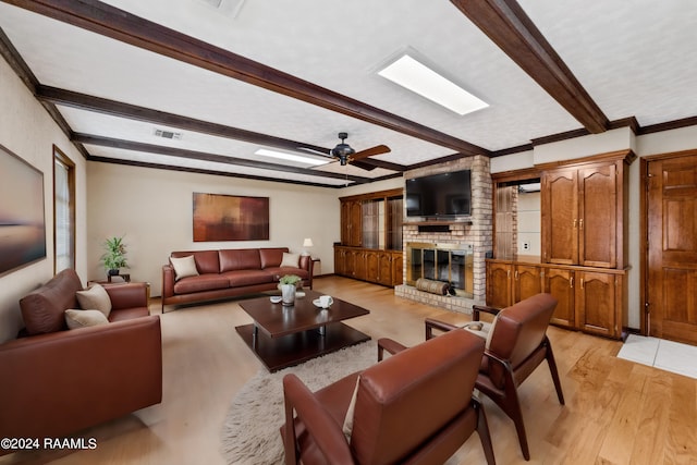 living room with a skylight, a brick fireplace, beamed ceiling, ceiling fan, and light hardwood / wood-style floors