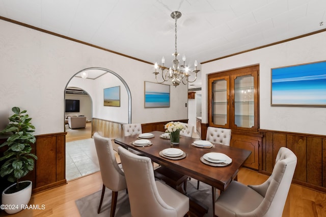 dining area with ornamental molding, a chandelier, light hardwood / wood-style flooring, and wood walls