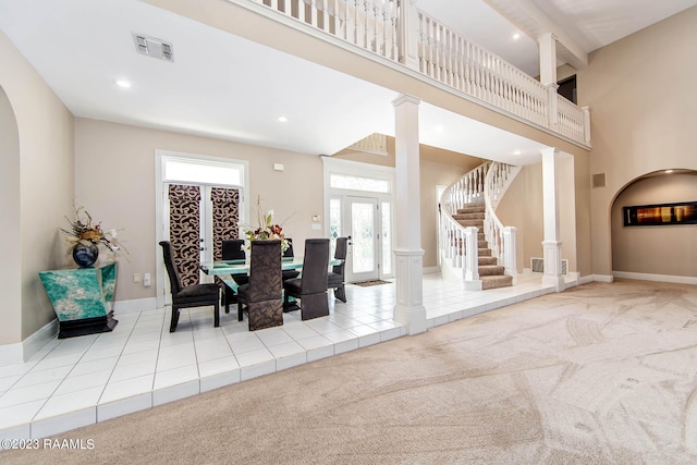 dining room featuring a high ceiling, decorative columns, beamed ceiling, french doors, and light colored carpet