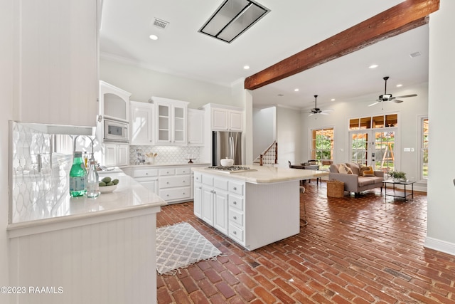 kitchen with stainless steel appliances, backsplash, ceiling fan, white cabinetry, and beamed ceiling