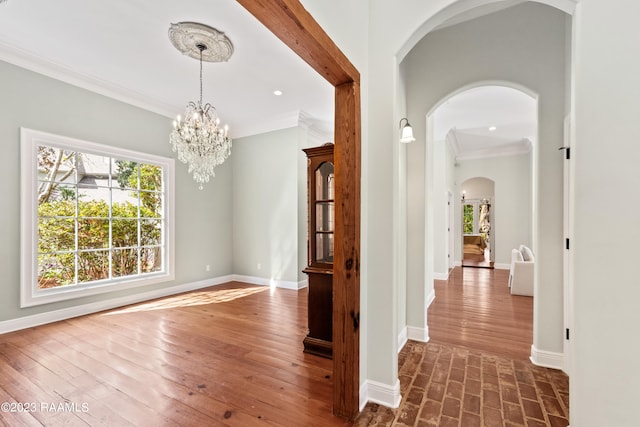 hallway featuring ornamental molding, dark wood-type flooring, plenty of natural light, and an inviting chandelier