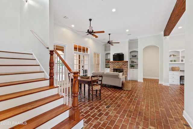 living room with a fireplace, ceiling fan, crown molding, built in shelves, and french doors