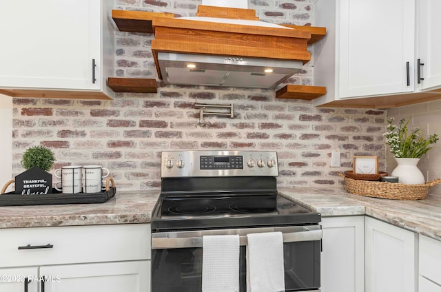 kitchen featuring light stone countertops, brick wall, stainless steel range with electric cooktop, and white cabinets