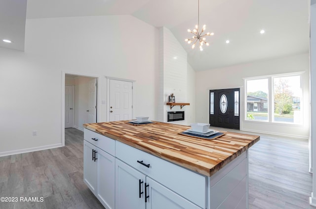 kitchen featuring butcher block countertops, high vaulted ceiling, light wood-type flooring, a center island, and a chandelier