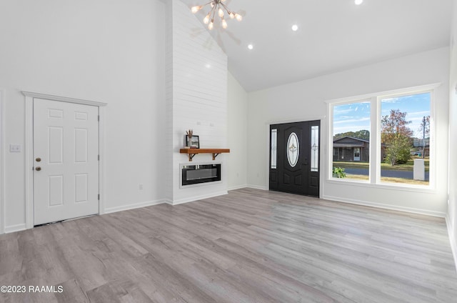 foyer entrance featuring an inviting chandelier, brick wall, light hardwood / wood-style flooring, high vaulted ceiling, and a large fireplace