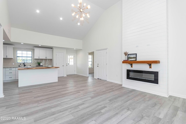 kitchen featuring a chandelier, light hardwood / wood-style floors, high vaulted ceiling, tasteful backsplash, and sink