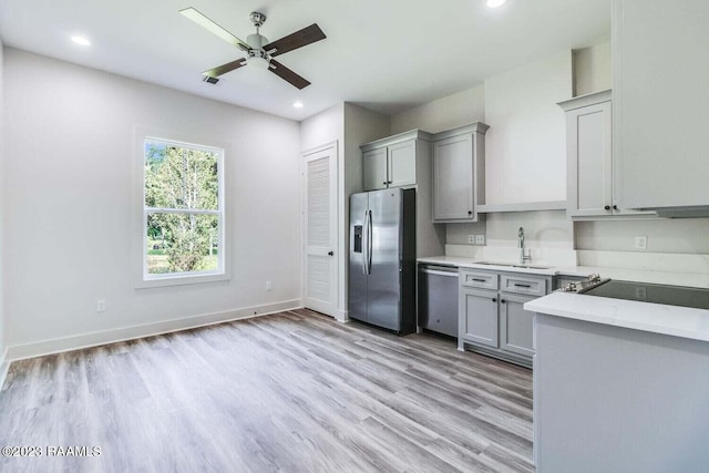 kitchen featuring light wood-type flooring, light stone counters, stainless steel appliances, sink, and ceiling fan