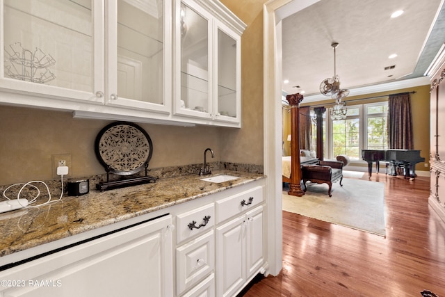 bar with sink, hanging light fixtures, crown molding, hardwood / wood-style floors, and white cabinets