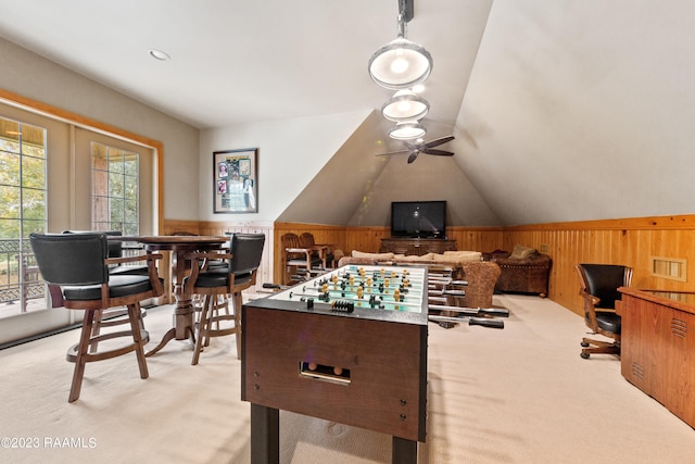 rec room featuring wooden walls, ceiling fan, light carpet, and vaulted ceiling