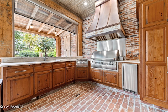 kitchen featuring sink, beamed ceiling, brick wall, stainless steel fridge, and custom exhaust hood