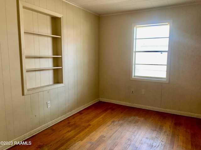 empty room with ornamental molding, dark hardwood / wood-style flooring, and built in shelves