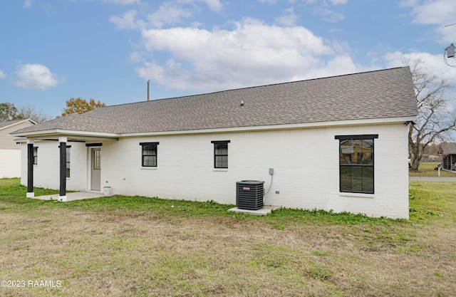 rear view of property with brick siding, central AC unit, a yard, and roof with shingles