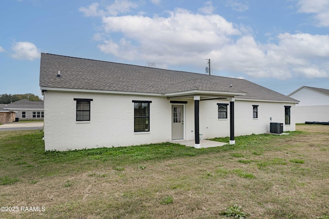 rear view of house featuring brick siding, a yard, and roof with shingles