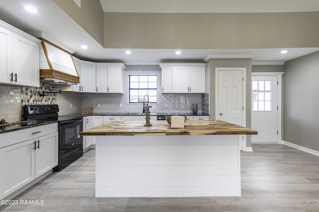 kitchen with premium range hood, wooden counters, a sink, black range with electric stovetop, and a center island