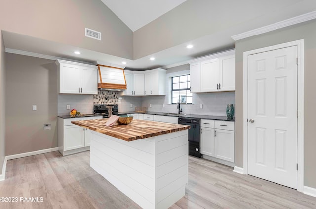 kitchen featuring wooden counters, custom range hood, white cabinets, a center island, and black appliances