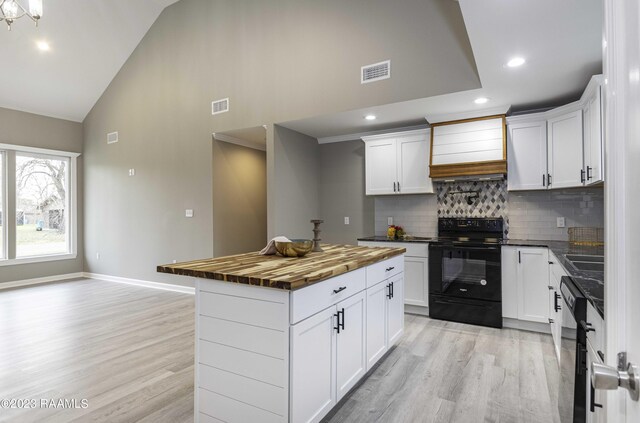 kitchen with decorative backsplash, black / electric stove, light hardwood / wood-style floors, and butcher block counters