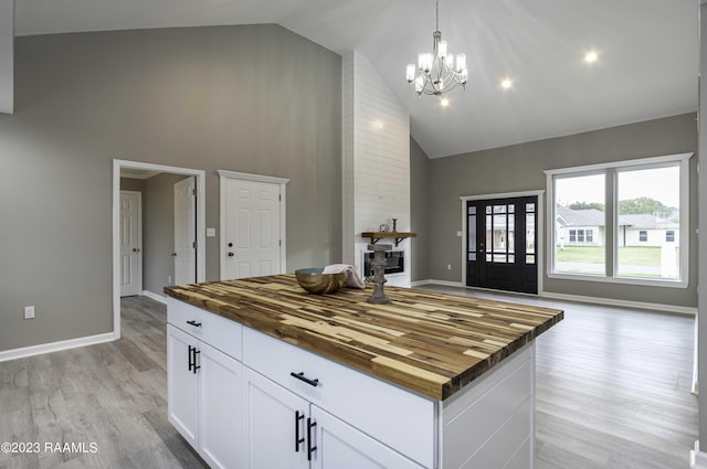 kitchen with high vaulted ceiling, white cabinets, light wood-style floors, wood counters, and decorative light fixtures