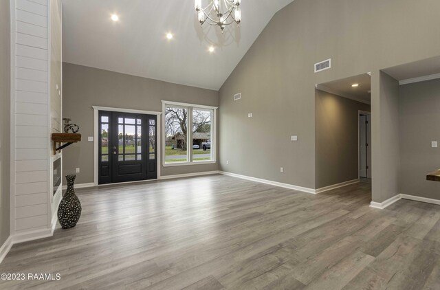 unfurnished living room featuring high vaulted ceiling, light hardwood / wood-style flooring, and a notable chandelier