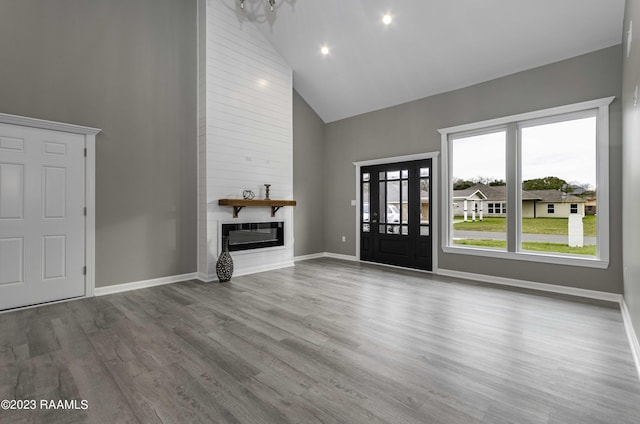 unfurnished living room with a fireplace, high vaulted ceiling, baseboards, and wood finished floors