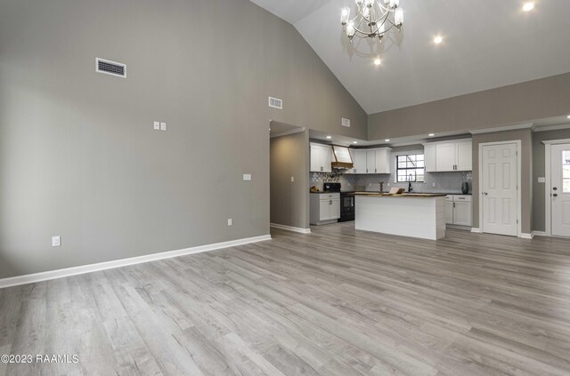 unfurnished living room with sink, high vaulted ceiling, a chandelier, and light hardwood / wood-style flooring