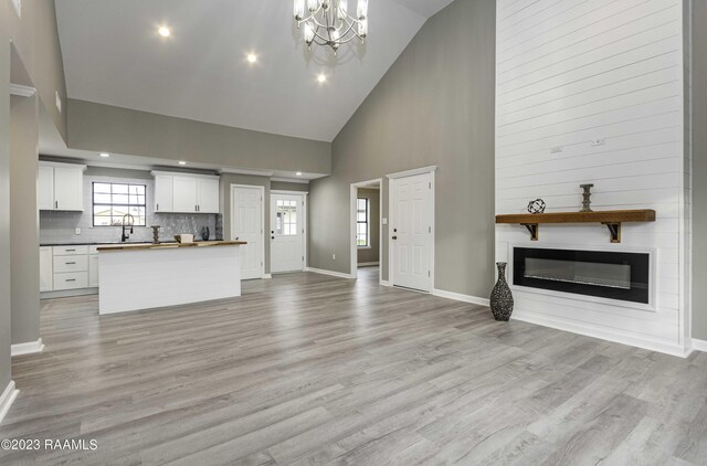 unfurnished living room featuring a notable chandelier, light hardwood / wood-style flooring, sink, and high vaulted ceiling