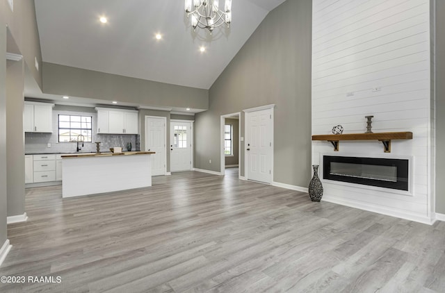 unfurnished living room with baseboards, a sink, light wood-style floors, a glass covered fireplace, and a chandelier