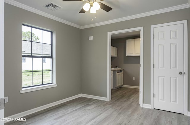 empty room featuring crown molding, light wood-style flooring, baseboards, and visible vents