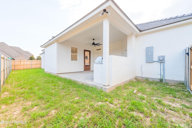 back of property with ceiling fan, a lawn, electric panel, and a patio area