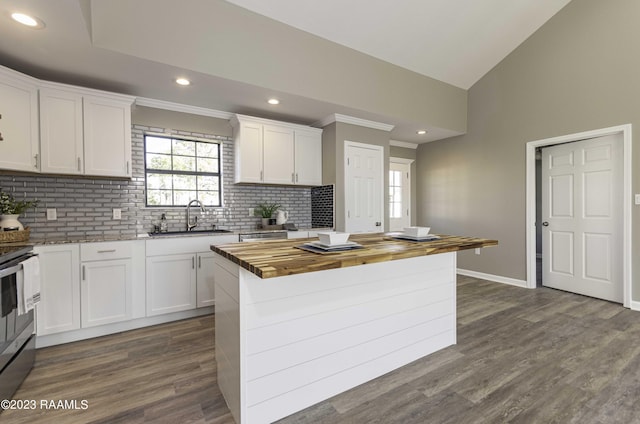 kitchen with butcher block countertops, a kitchen island, white cabinetry, and sink