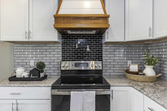 kitchen featuring custom exhaust hood, white cabinets, electric range, tasteful backsplash, and light stone counters